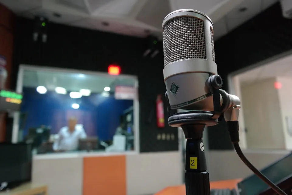 Micrófono de condensador en un estudio, con la sala de control al fondo.