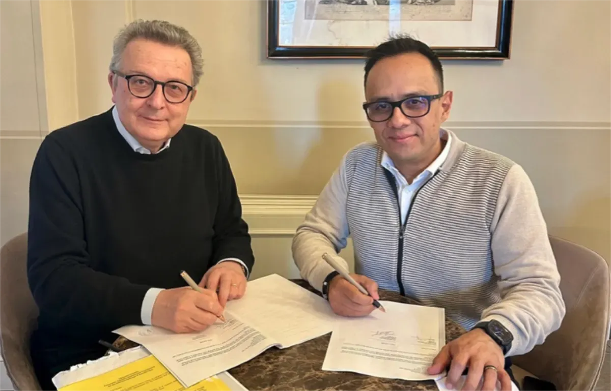 Dos representantes firman documentos sentados a una mesa.