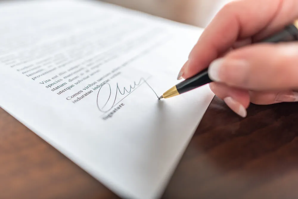 Mano firmando un contrato con una pluma.