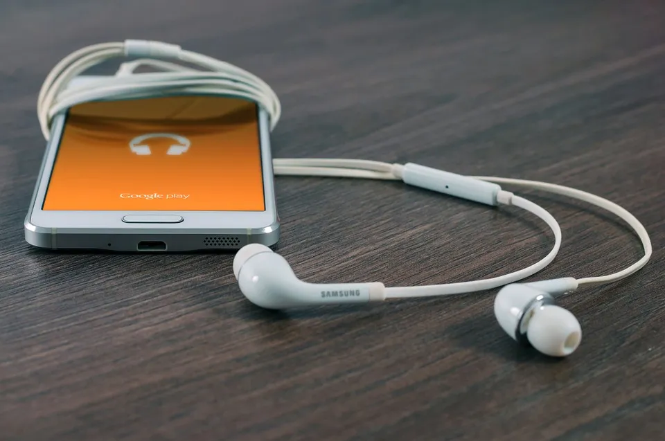 Teléfono con una aplicación de música y audífonos sobre una mesa de madera.