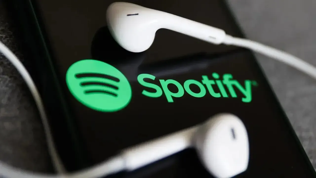 Logo de Spotify en la pantalla de un teléfono con audífonos blancos.